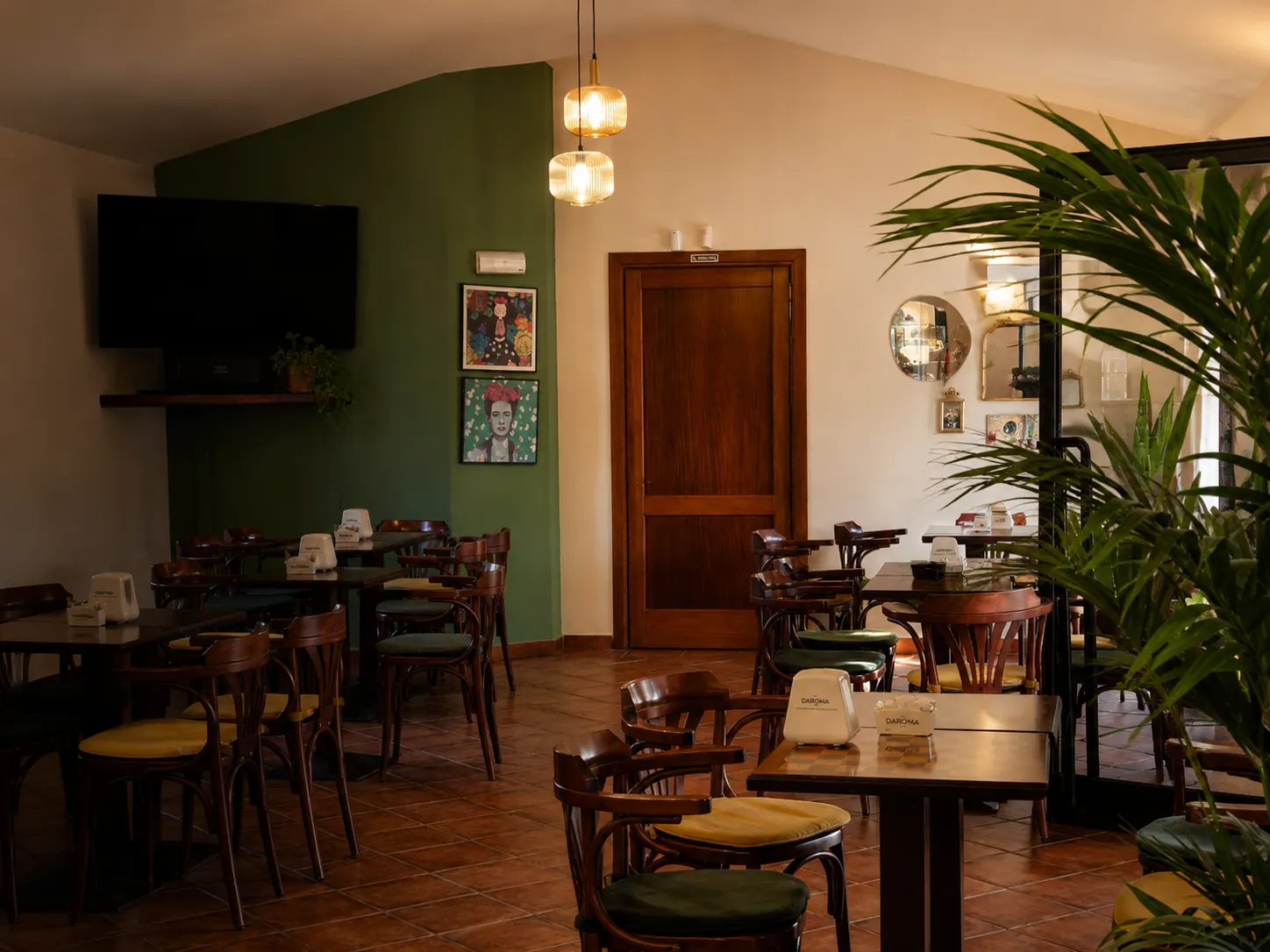 Sala interna del caffè con tavolini e sedie in legno, parete verde, porta in legno e lampade a sospensione